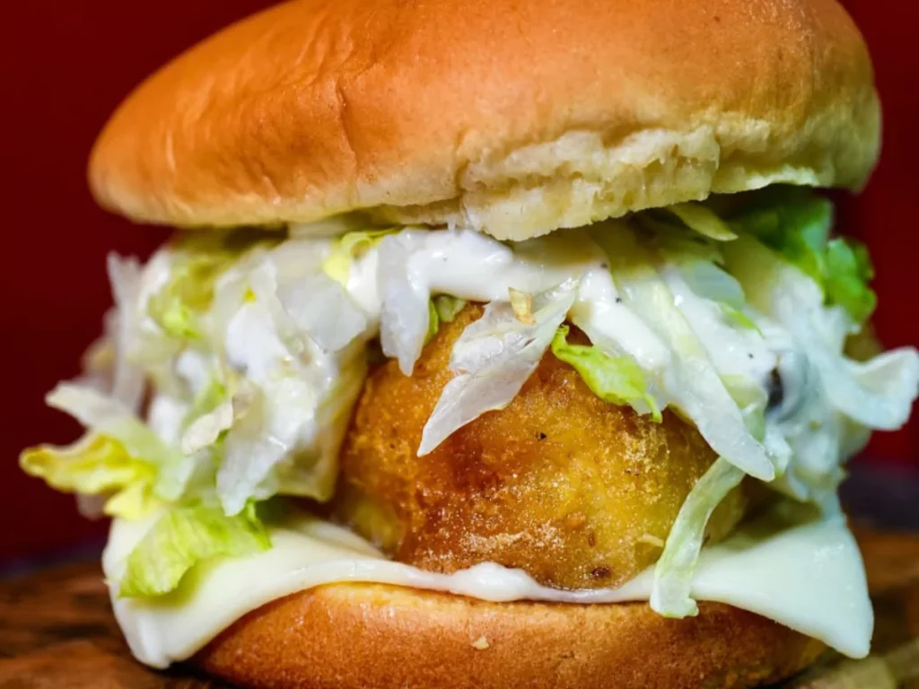 Close-up of crispy fried patty in 24 hour burgers in Kingsbridge Place, with fresh lettuce, creamy sauce, and melted cheese on a soft bun