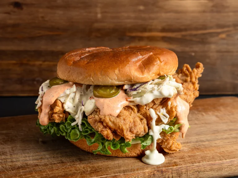Tasty affordable burgers in Sugar Land TX with fried chicken, coleslaw, jalapeños, and creamy sauce on a bun