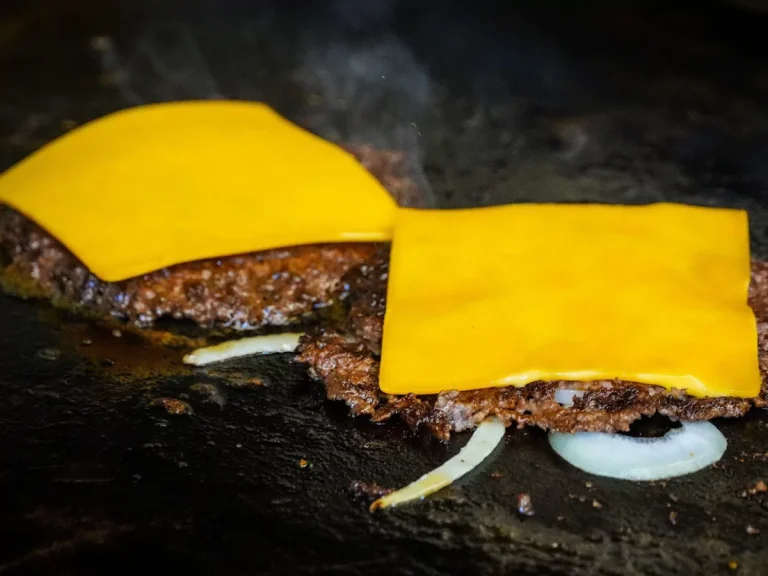 Two smash burger patties cooking on a griddle, each topped with a slice of melting American cheese, a typical sight at Sugar Land Burger Joints