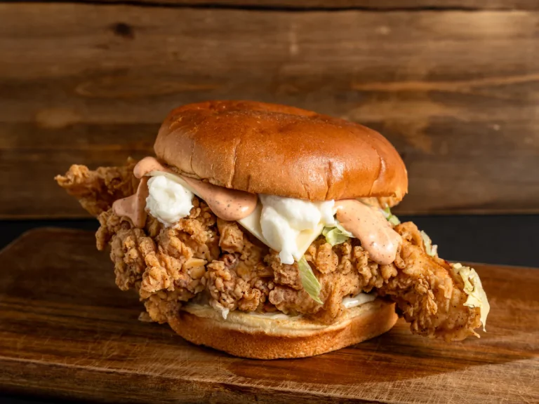Crispy chicken burger in Sugar Land with lettuce and creamy sauce on a toasted bun on wood