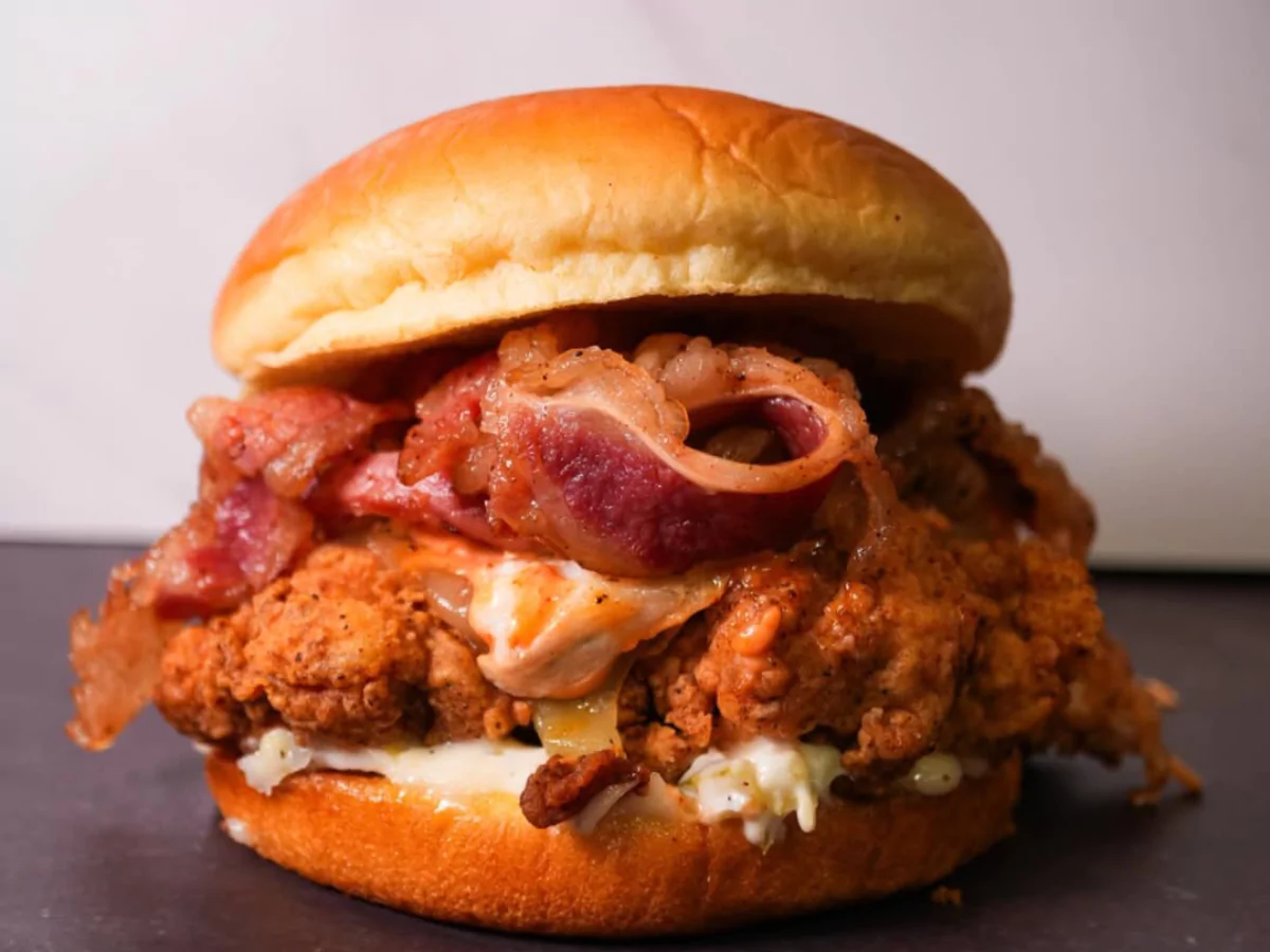 Close-up of late night burger delivery in Woodbridge Estates with fried chicken, melted cheese, bacon, and creamy sauce on a soft bun