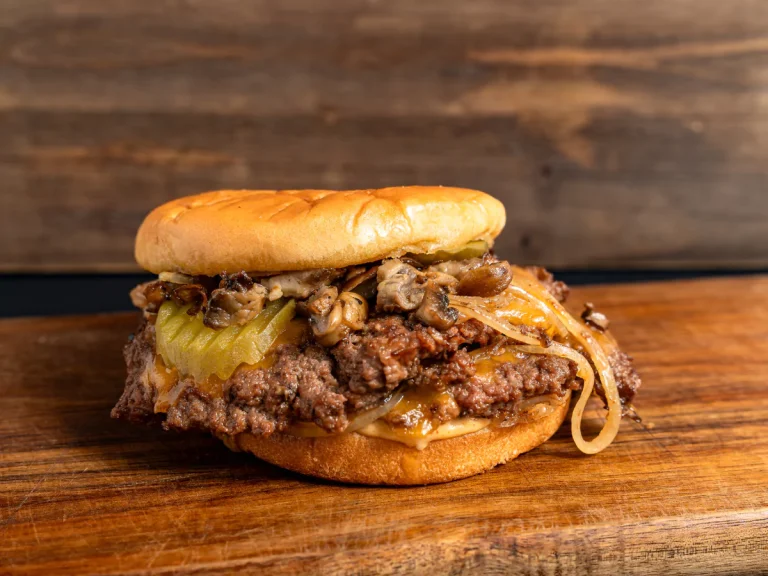 A loaded cheeseburger with sautéed onions, mushrooms, and pickles on a toasted bun, a perfect craving-killer for late night burgers in Sugar Land