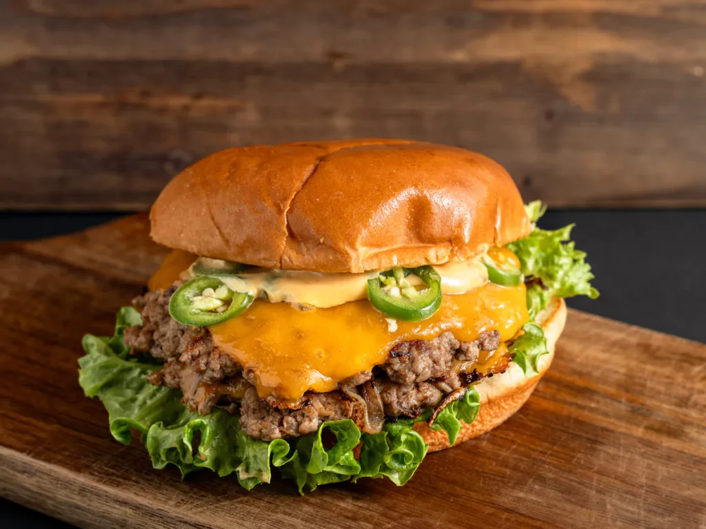 Gourmet smash burger with melted cheddar cheese, chopped beef, sautéed onions, fresh lettuce, and jalapeños on a toasted brioche bun, the kind of quality you find in local burgers near Sugar Land