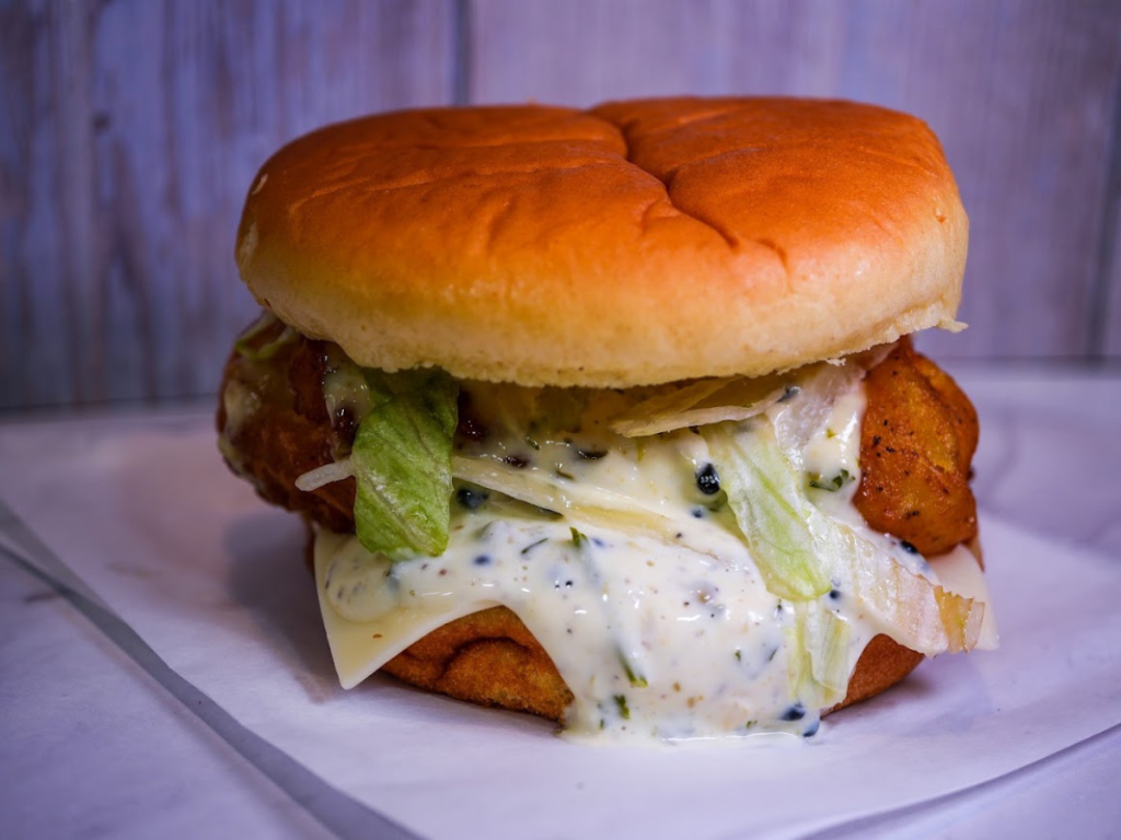 A generously sauced chicken sandwich on a brioche bun with lettuce and cheese, showcasing delicious options available at Sugar Land Burger Joints