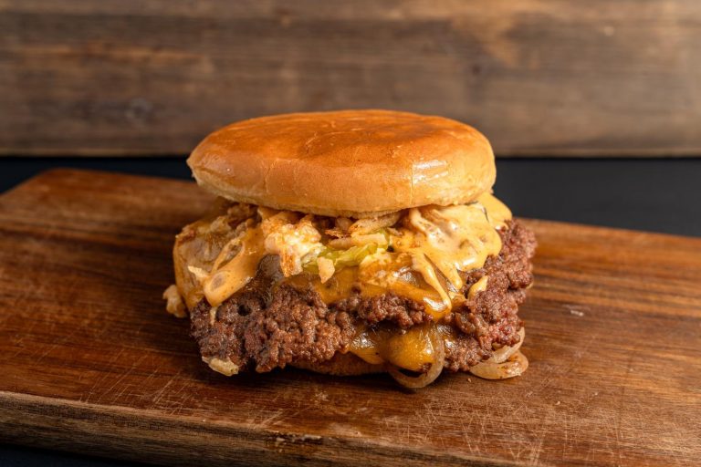 Juicy double burger with melted cheese, onion rings, and pickles at top burger restaurants in Sugar Land.