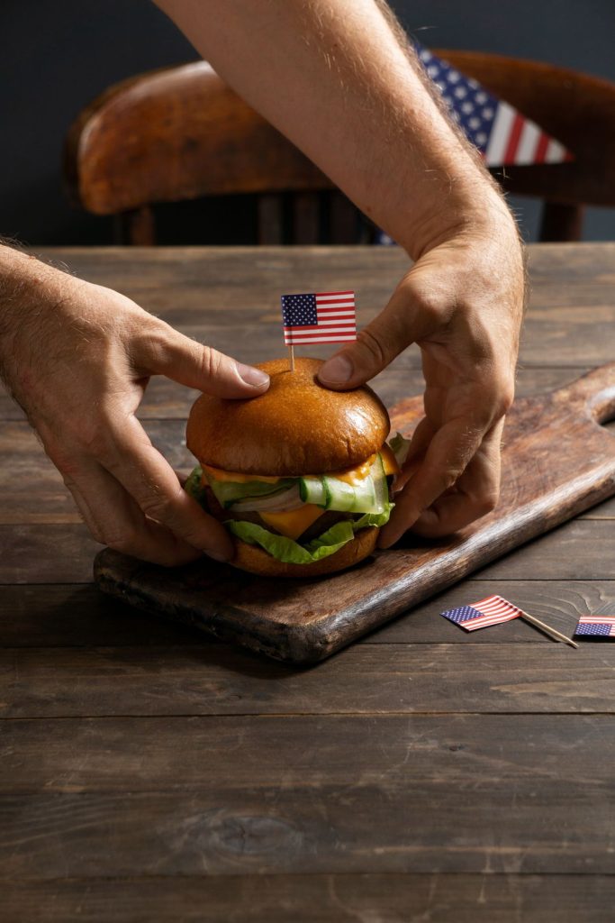 Hands holding a delicious chicken burger with lettuce and cheese, topped with an American flag, served in Sugar Land.