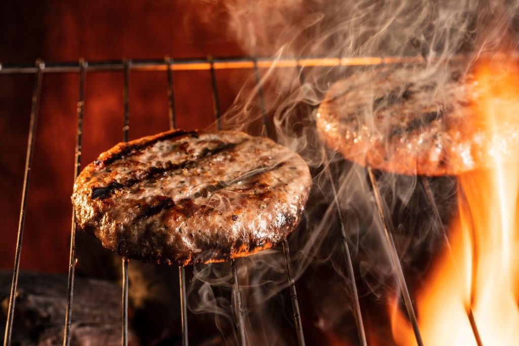 Juicy burgers sizzling on a grill with smoke, paired with loaded fries in Sugar Land for a savory meal.