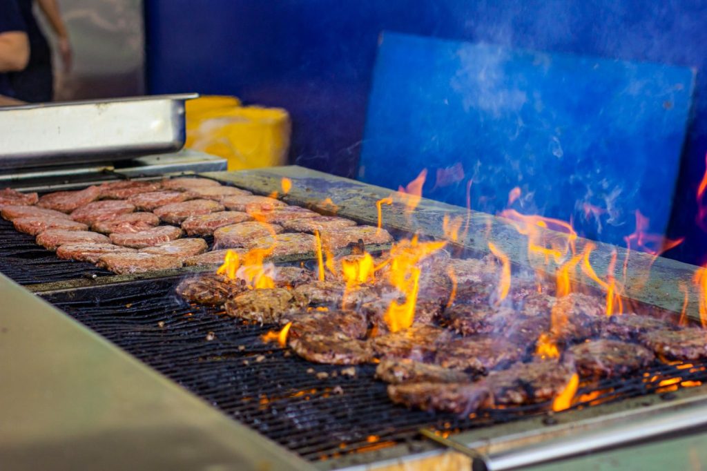 Flaming beef patties grilling with intense fire at burger restaurants Sugar Land, delivering smoky and juicy flavors for burger lovers.