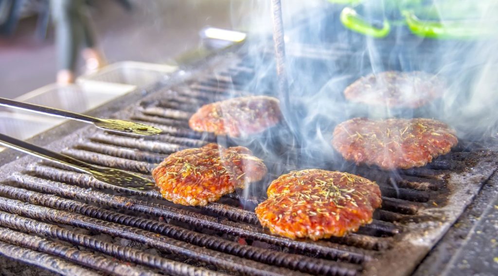 Herb-seasoned beef patties steaming on the grill with tongs ready at burger restaurants Sugar Land, showcasing fresh and flavorful options.