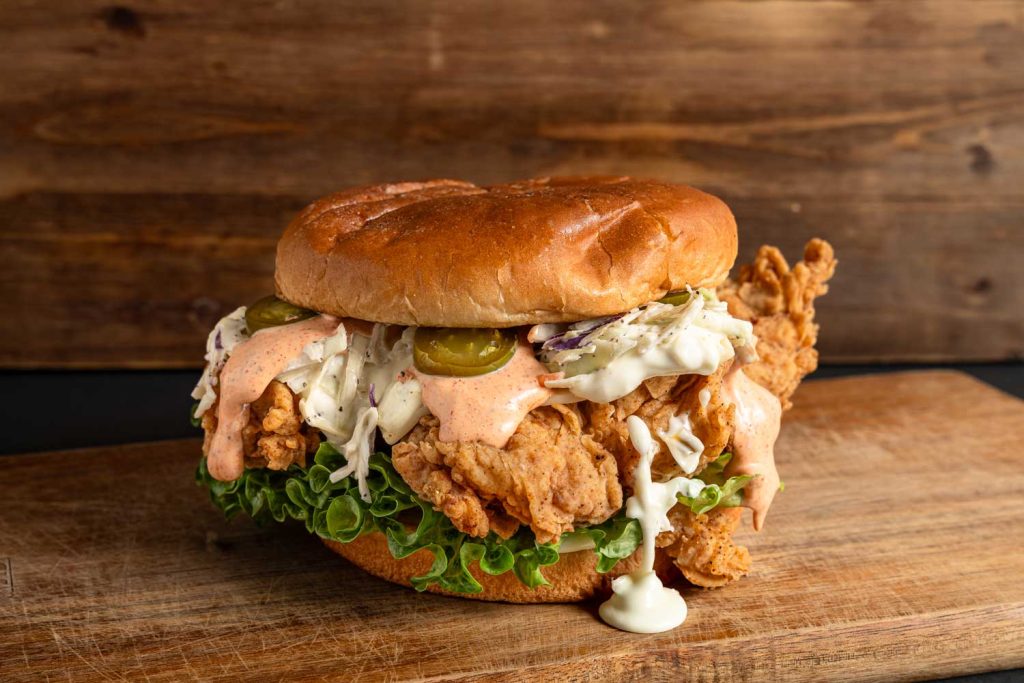 Juicy affordable burger with crispy chicken, coleslaw, and jalapenos on a bun, served in Sugar Land, TX.