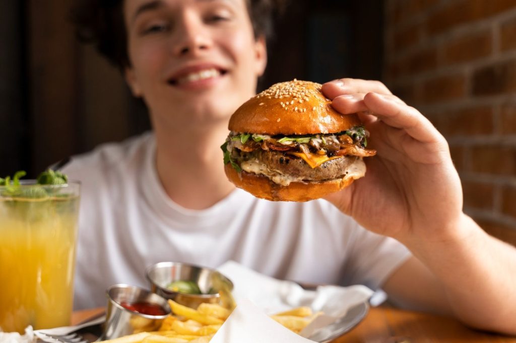 Smiling person holding juicy affordable burger with bacon, cheese, and veggies in Sugar Land, TX, enjoying fries and drink at casual dining spot.