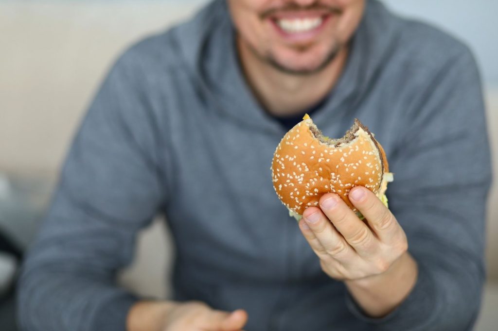 Happy man biting into sesame-seed affordable burger in Sugar Land, TX, showcasing fresh layers of patty, cheese, and toppings for budget-friendly meals.