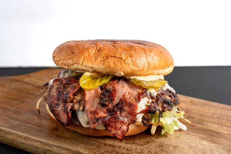 Juicy best burgers in Sugar Land served on a wooden board with pickles, lettuce, and melted cheese in a tasty stack.