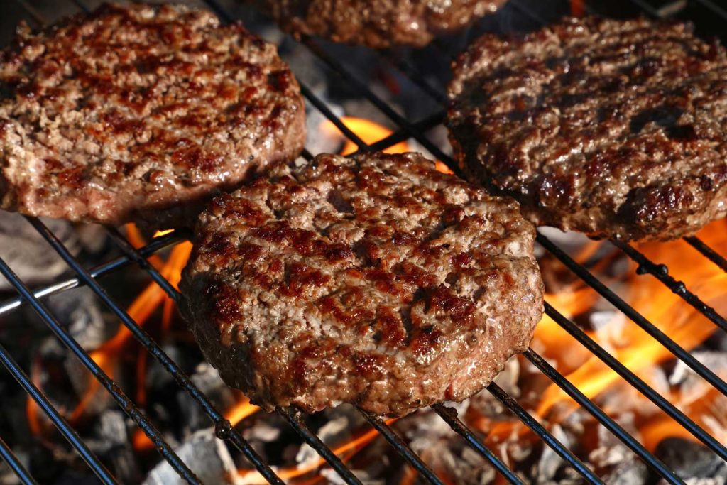 Freshly grilled patties for the best burgers in Sugar Land cooking over an open flame on a barbecue grill.