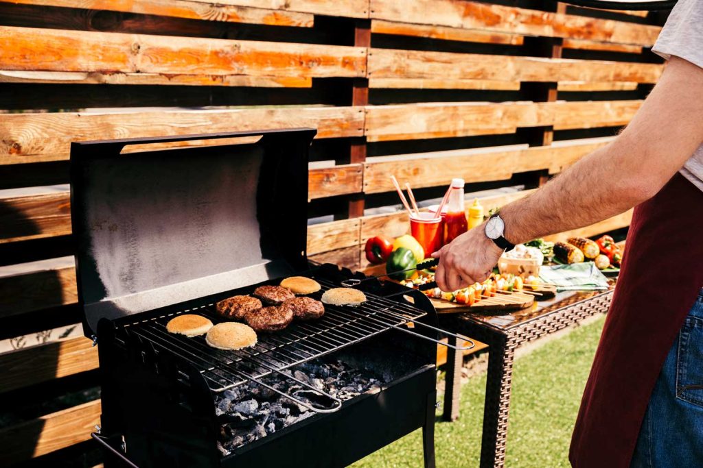 Chef grilling delicious best burgers in Sugar Land with fresh veggies and condiments on a table beside a wooden fence.
