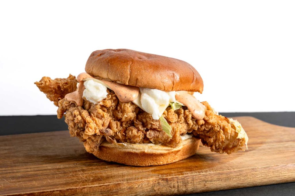 Crispy fried chicken burger topped with creamy white and pink sauces on a soft bun, affordable in Sugar Land, TX.